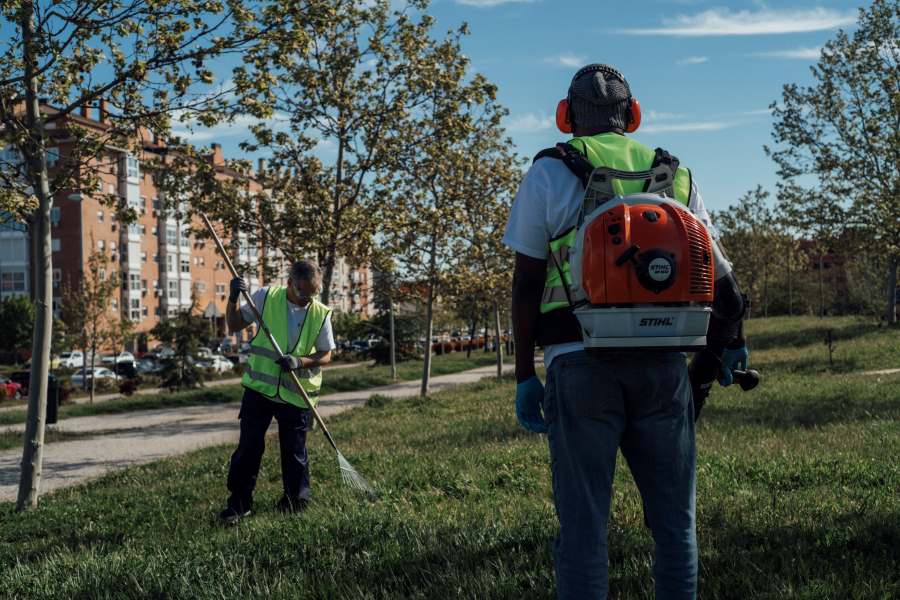 Trabajadores de mantenimiento de áreas verdes con soplador de hojas y rastrillo.